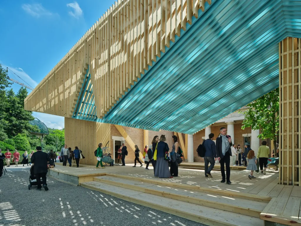 Low-angle view looking under the turquoise-lined underside of the slatted timber porch, showing visitors walking across the elevated wooden deck.