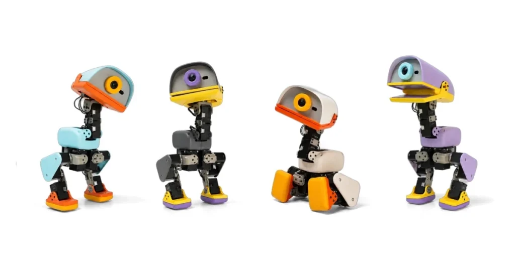 Four Microduck robots in different colours (blue, grey, cream and purple) standing in a row against a white background