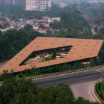 Overhead aerial of the angular, terracotta-tiled roof of Mitte Oblique Garden featuring a large irregular central opening, multiple circular roof vents, and visible landscaped interior spaces below.