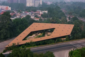 Overhead aerial of the angular, terracotta-tiled roof of Mitte Oblique Garden featuring a large irregular central opening, multiple circular roof vents, and visible landscaped interior spaces below.