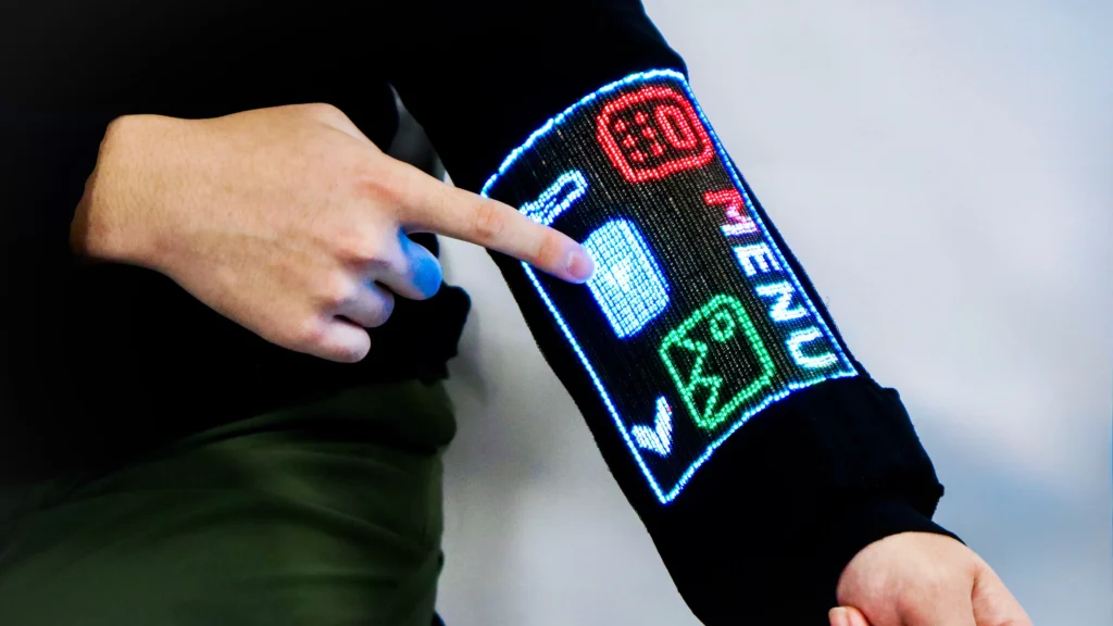 Close-up of a hand tapping a glowing menu interface displayed on the black sleeve, showing colourful icons including a calculator and temperature symbol
