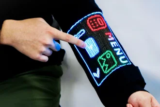 Close-up of a hand tapping a glowing menu interface displayed on the black sleeve, showing colourful icons including a calculator and temperature symbol