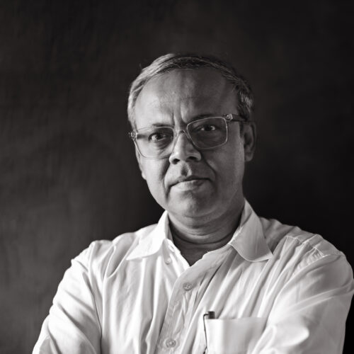 Black-and-white portrait of architect Bayejid Khondoker wearing glasses and a white shirt, arms crossed