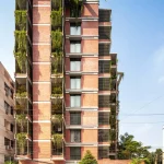 Red-brick residential tower with cascading greenery spilling from balconies and terraces along a city street