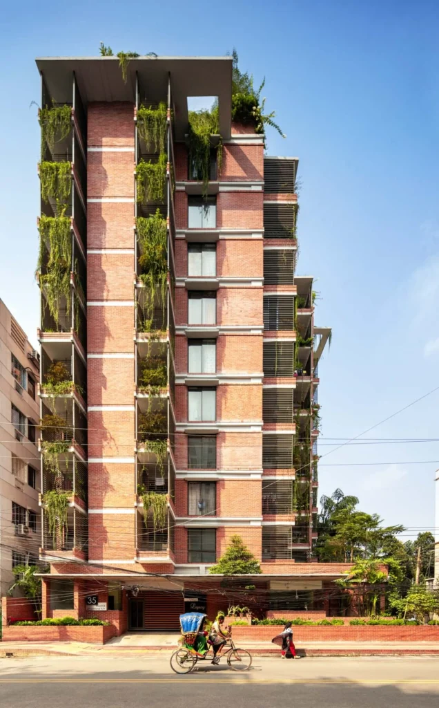 Red-brick residential tower with cascading greenery spilling from balconies and terraces along a city street