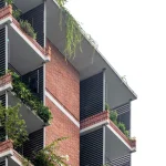 Close-up of red-brick residential façade with deep balconies, horizontal louvres and abundant hanging greenery