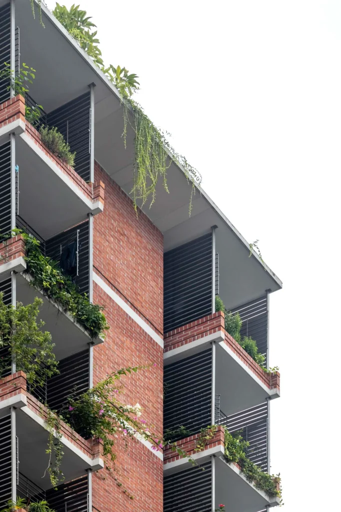 Close-up of red-brick residential façade with deep balconies, horizontal louvres and abundant hanging greenery