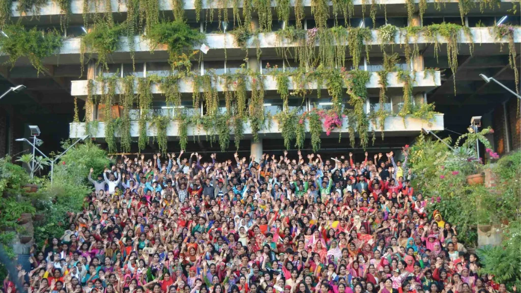 Large group of workers in colourful clothing raising their hands in front of a multi-storey building covered in hanging greenery