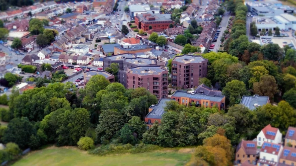 Aerial view of five brick residential blocks set among trees and green space in a suburban London setting