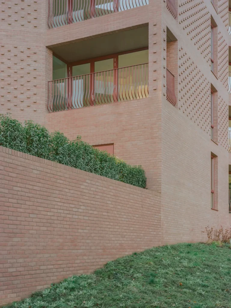 Close-up of a textured brick facade with projecting details, wavy metal balcony railings and planting