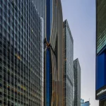 A tall, slender skyscraper with bronze fluid vertical fins and integrated accent lighting towering above a busy city street in Hong Kong.