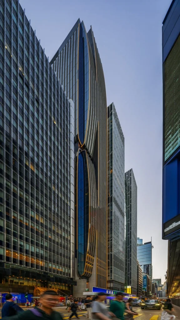 Aedas Turns Historic Takshing House into a Fluid Central Icon_A tall, slender skyscraper with bronze fluid vertical fins and integrated accent lighting towering above a busy city street in Hong Kong.