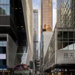 Street-level view framed by tall city buildings looking down a dense pedestrian street toward a gleaming golden-hued high-rise tower.