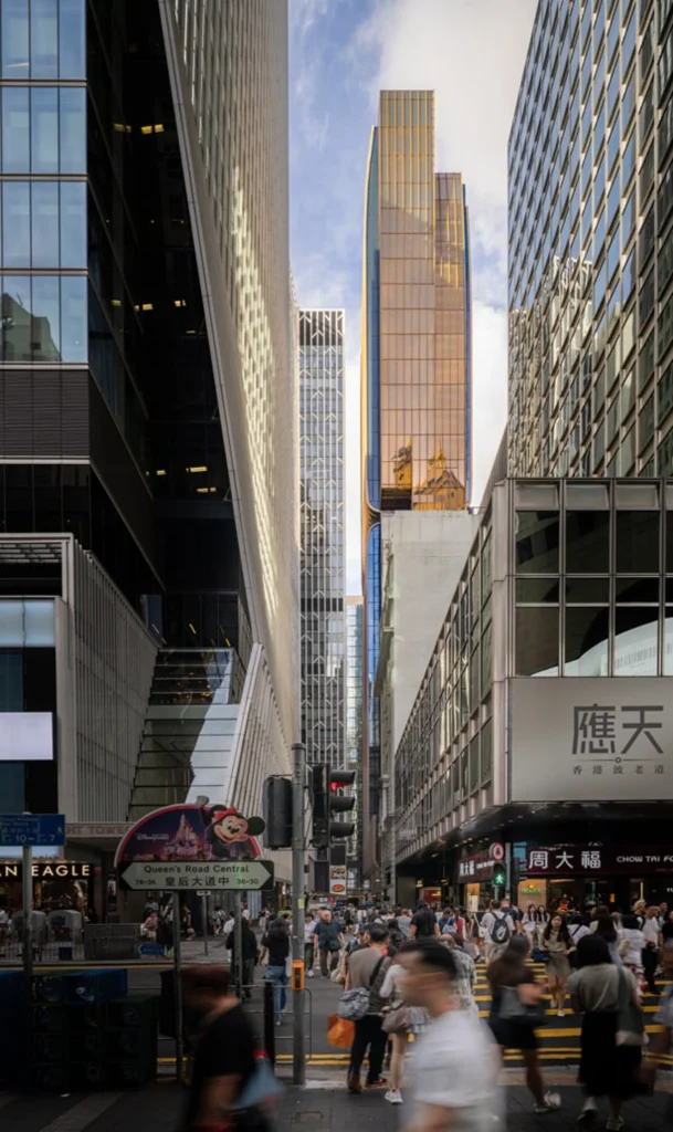 Street-level view framed by tall city buildings looking down a dense pedestrian street toward a gleaming golden-hued high-rise tower.