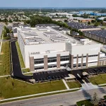 Aerial view of a data center building with rooftop cooling equipment, electrical infrastructure, and surrounding commercial developments