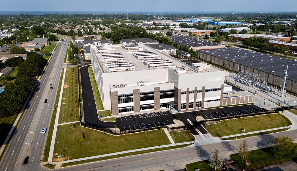 Aerial view of a data center building with rooftop cooling equipment, electrical infrastructure, and surrounding commercial developments