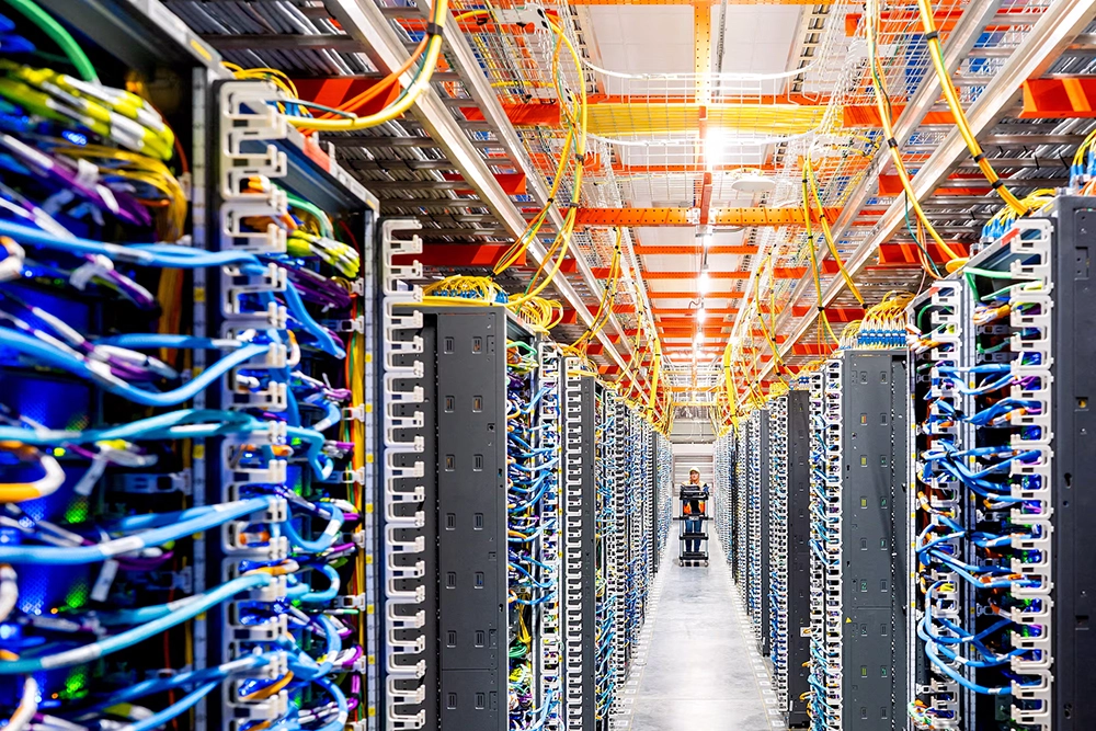 Interior of an AI data center with densely arranged server racks, colorful network cables, and overhead cable management systems for high-performance computing