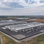 Aerial view of a large data center complex in a rural landscape, featuring multiple low-rise buildings, rooftop mechanical equipment, and secured infrastructure