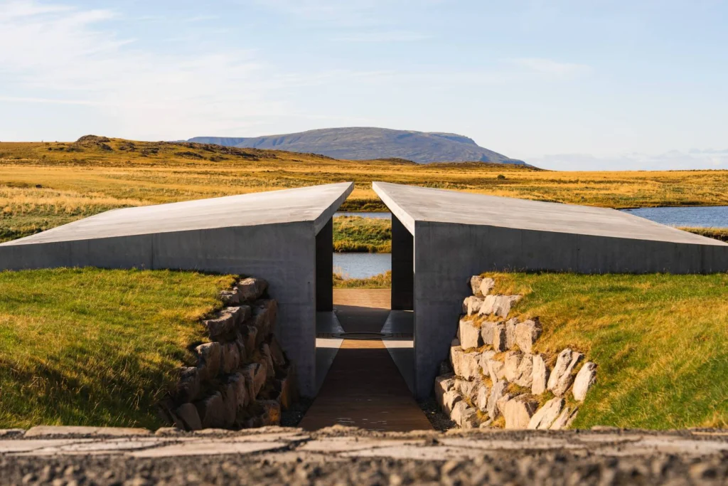 View through the concrete Temple’s central opening toward a lake and distant mountain under a clear sky