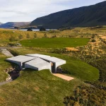 Aerial view of the cross-shaped concrete Temple set into green and golden hillside near a lake