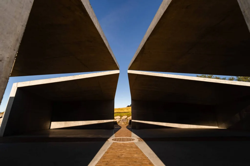 Low-angle view upward between concrete roof planes toward blue sky and a narrow path of light