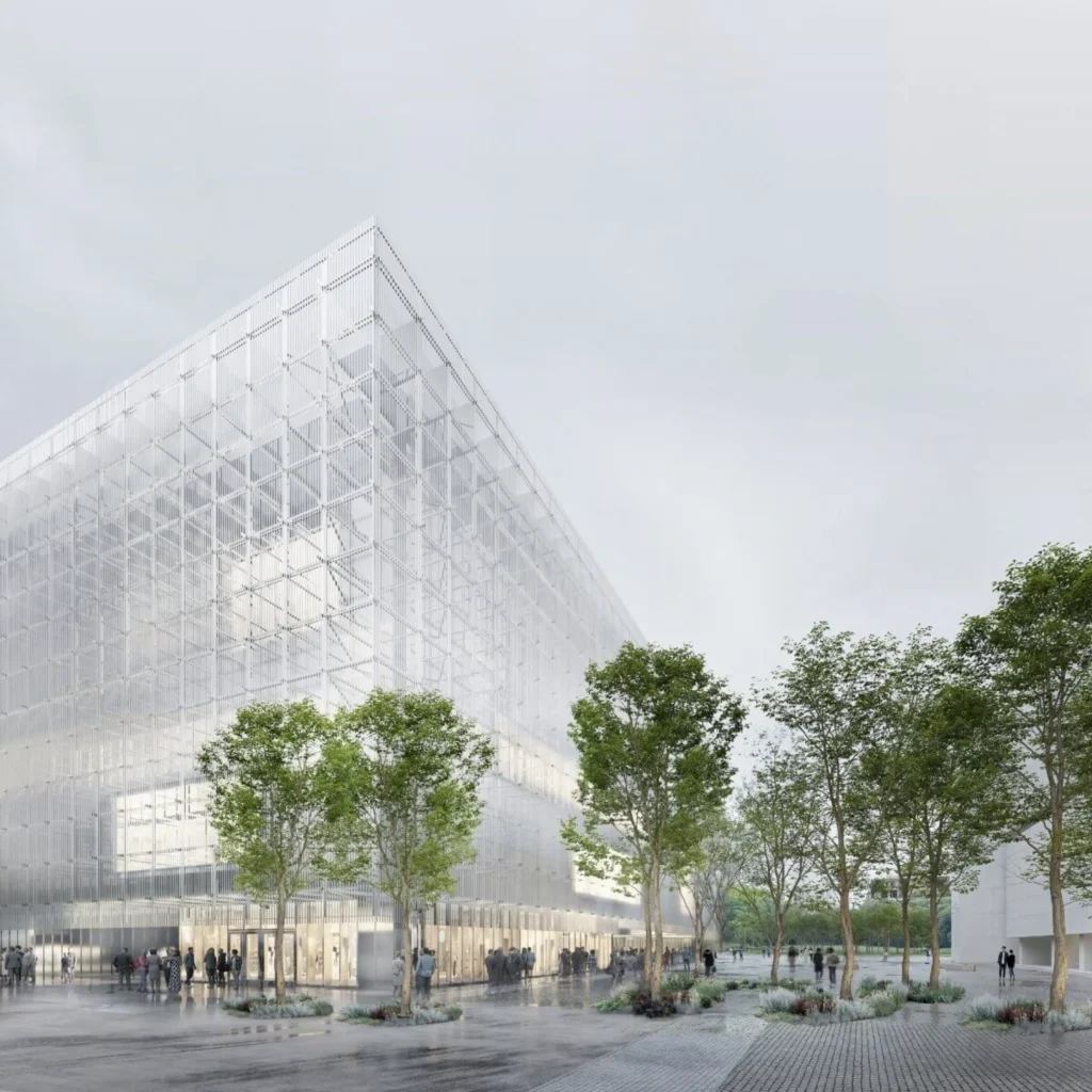 Angular view of the tall translucent gridded façade rising above a paved public space lined with trees