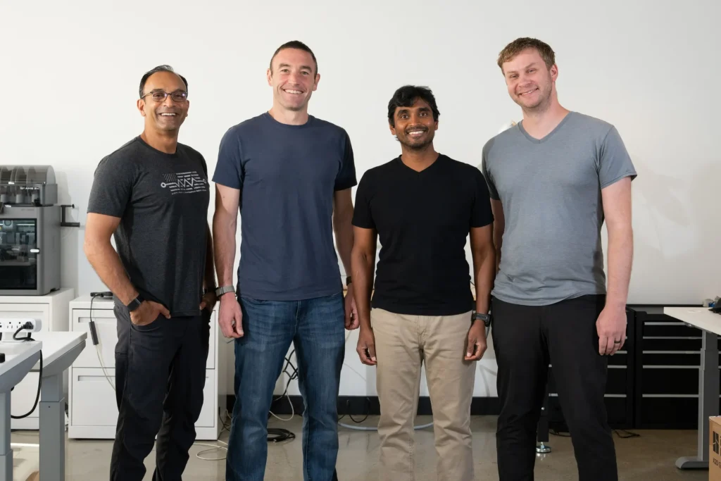 Four co-founders of Warp Sciences standing side by side in a modern office laboratory space, smiling at the camera