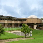 Distant view of the planetarium dome and surrounding Polk Science Building framed by roses and greenery