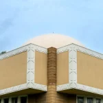Low-angle view looking up the corner of the building with patterned textile blocks and a vertical masonry pier against the sky