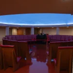 Circular interior of the restored planetarium with red vinyl seating arranged around a central projector under a blue-lit dome