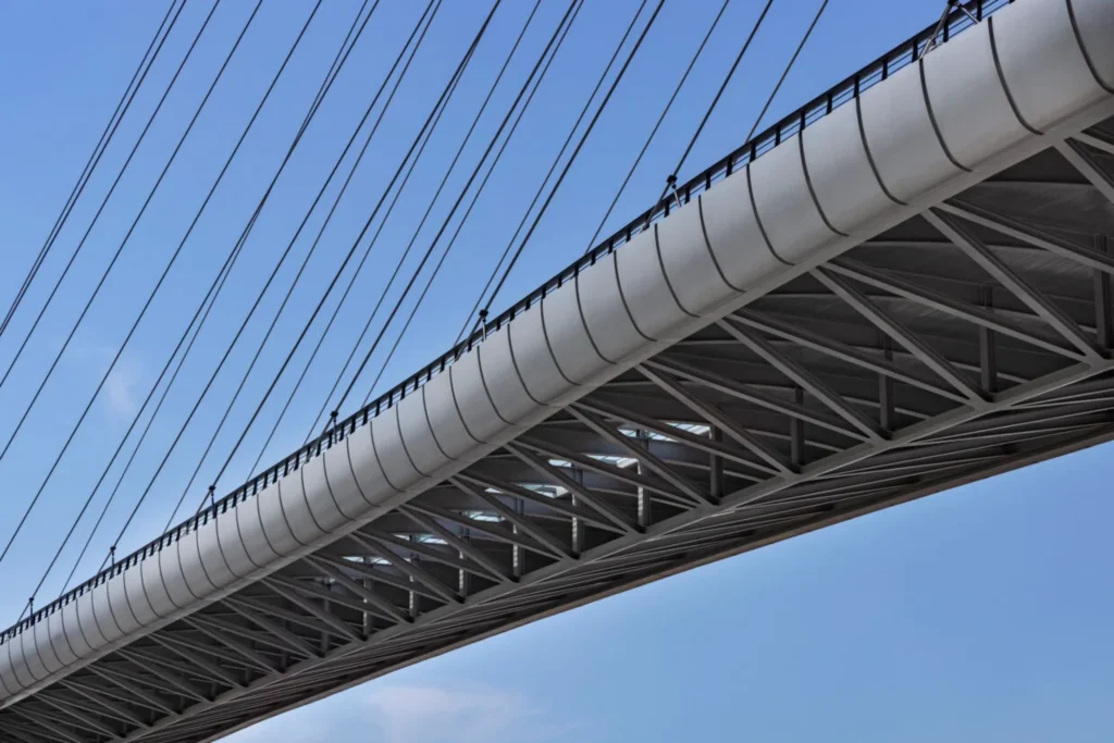 Close-up underside of the bridge deck showing the white steel truss structure and radiating stay cables against a blue sky