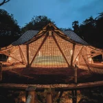 Night view of a glowing bamboo pavilion with lattice walls and sweeping roof illuminated from within