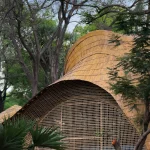 Bamboo pavilion with undulating roof beside a multi-tiered stone fountain
