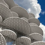 Close-up of stacked perforated white disks against a blue sky with scattered cloudsClose-up of stacked perforated white disks against a blue sky with scattered clouds