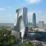 Close aerial of the twisting triangular-panelled glass tower with rooftop terrace and surrounding streets