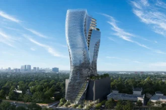 Aerial view of the sinuous glass O27 tower rising above a dark podium amid green surroundings and distant Houston skyline