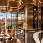 Grand double-height lobby with curved bronze walls, marble columns, reception desk and soft seating