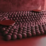 Soft undulating field of deep maroon rounded forms with two flat circular platforms resting on top