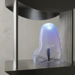 Translucent pale purple glass-like form resting on a metal shelf between two curved dark metal plates