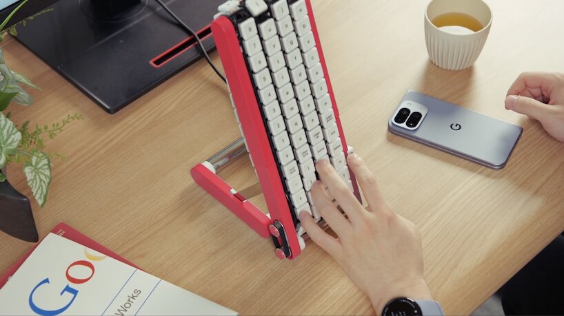 Overhead view of a red Gboard keyboard on a desk beside a phone, tea cup and Google notebook