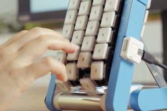Hand pressing keys on the blue conveyor-belt keyboard as the keys move past the fingers