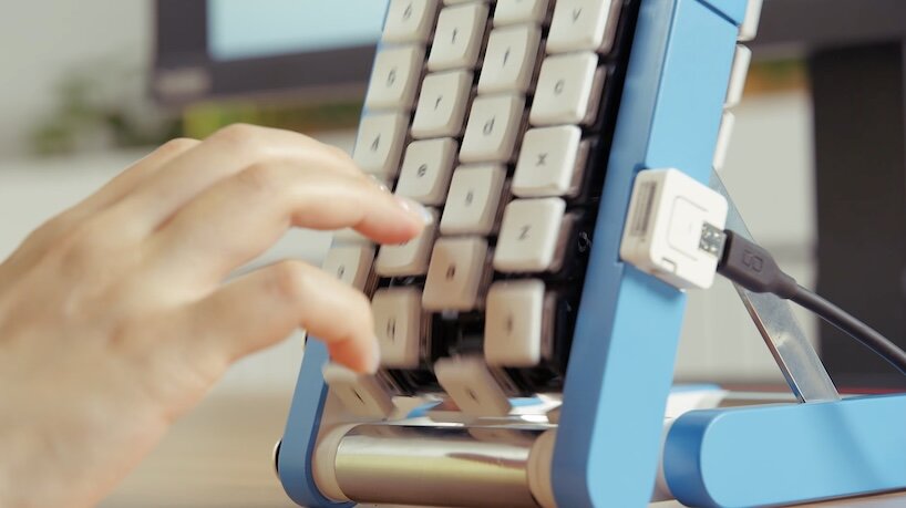 Hand pressing keys on the blue conveyor-belt keyboard as the keys move past the fingers