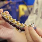 Close-up of hands holding a flexible circuit strip with small rollers and electronic components
