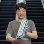 Smiling man holding the blue Gboard conveyor-belt keyboard in front of an escalator