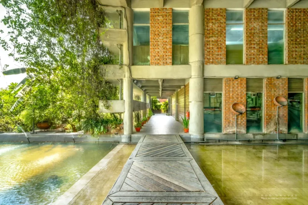 Covered walkway beside a reflecting pool with brick and concrete structure