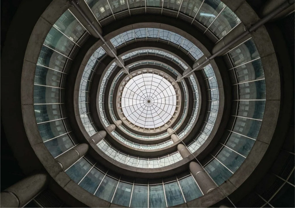 Looking straight up into a multi-storey circular atrium with concentric concrete rings and a glazed skylight