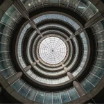 Looking straight up into a multi-storey circular atrium with concentric concrete rings and a glazed skylight