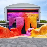 Front view of large LEGO flower wave sculptures in red, orange, yellow and purple standing before the TANK Shanghai facade