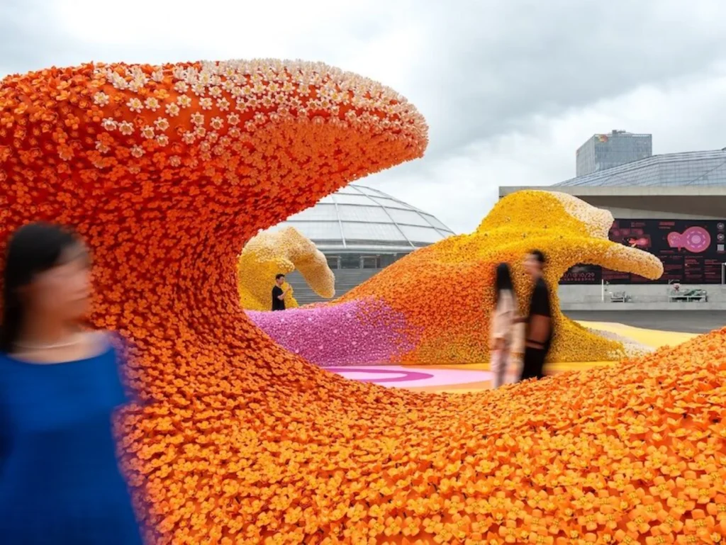 Close-up of a dense orange LEGO flower wave with visitors walking nearby under an overcast sky