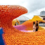Close-up of a dense orange LEGO flower wave with visitors walking nearby under an overcast sky